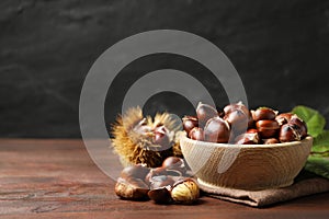 Delicious roasted edible chestnuts in bowl on wooden brown table. Space for text