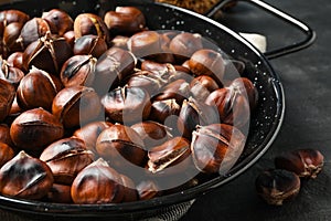 Delicious roasted edible chestnuts in frying pan on black table, closeup