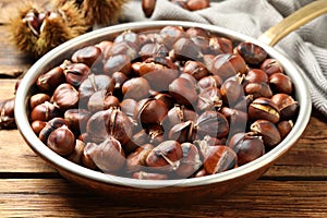 Delicious roasted edible chestnuts in frying pan on wooden table, closeup