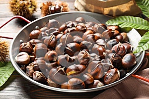 Delicious roasted edible chestnuts in frying pan on wooden table, closeup