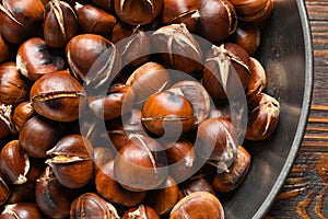 Delicious roasted edible chestnuts in frying pan on wooden table, top view