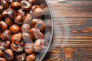 Delicious roasted edible chestnuts in frying pan on wooden table, top view. Space for text