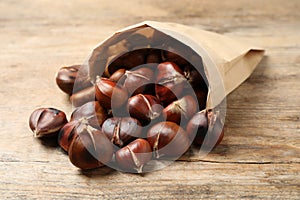 Delicious roasted edible chestnuts in paper bag on wooden table, closeup