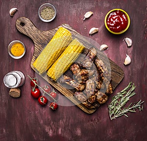 Delicious roasted lamb ribs with hot sauce, on a branch with tomatoes, roasted corn, spices, wooden rustic background top view