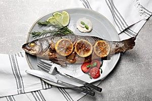 Delicious roasted sea bass fish served with lemon, rosemary and sauce on light grey table, flat lay