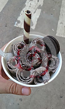 Delicious rolled ice cream with chocolate, oreo cookie and strawberry sauce in a cup