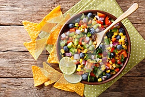 delicious salad of corn, blueberries, jalapeno pepper, bell pepper and onions is served with nachos chips close-up. horizontal to