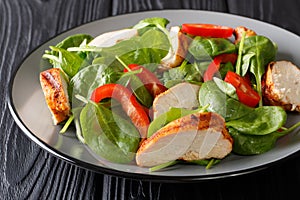 Delicious salad of fresh baby spinach, chicken breast and bell pepper close-up on a wooden table. horizontal