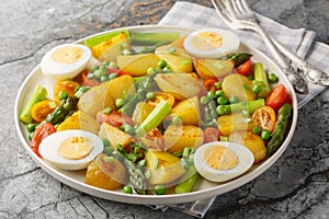 Delicious salad of potatoes, asparagus, cherry tomatoes, eggs and green peas close-up in a plate. Horizontal
