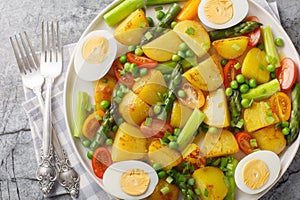 Delicious salad of potatoes, asparagus, cherry tomatoes, eggs and green peas close-up in a plate. Horizontal top view