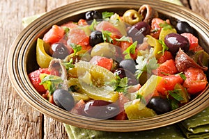 Delicious salad of tomatoes and green peppers Chlada felfel with anchovies and olives close-up in a bowl. horizontal