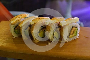 delicious salmon tempura and avocado sushi roll topped with sauce and cheese