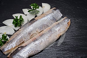 Delicious Salted Herring garnished with Yellow Onion slices and Fresh Parsley. Natural black stone. Clupea harengus.