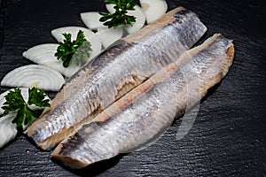 Delicious Salted Herring garnished with Yellow Onion slices and Fresh Parsley. Natural black stone. Clupea harengus.