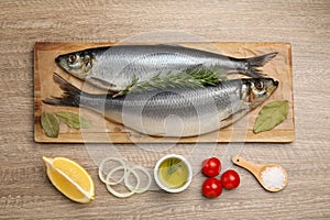 Delicious salted herrings and ingredients on wooden table, flat lay