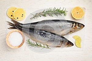 Delicious salted herrings, rosemary, salt and lemon on white wooden table, flat lay