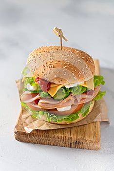 Delicious sandwich with fresh vegetables, cheese and ham on wooden board on gray background. Side view, close up. Menu, recipe