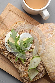 Delicious sandwich with tuna, boiled egg, vegetables and cup of tea on light grey table, flat lay