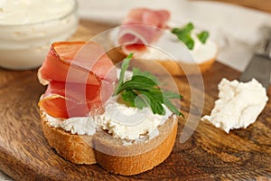 Delicious sandwiches with cream cheese and jamon on wooden board, closeup
