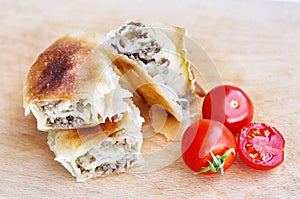 Delicious savory strudel stuffed with pork meat served on a wooden plate,with garlic and tomato cherry