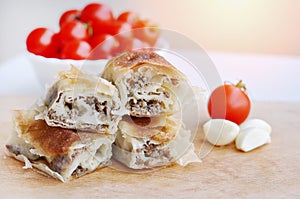 Delicious savory strudel stuffed with pork meat served on a wooden plate,with garlic and tomato cherry