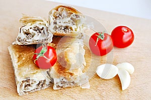 Delicious savory strudel stuffed with pork meat served on a wooden plate,with garlic and tomato cherry