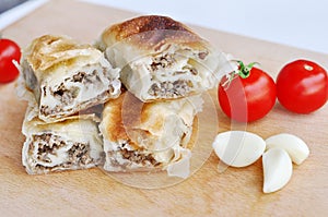 Delicious savory strudel stuffed with pork meat served on a wooden plate,with garlic and tomato cherry