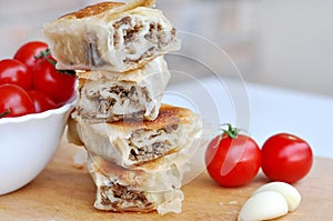 Delicious savory strudel stuffed with pork meat served on a wooden plate,with garlic and tomato cherry