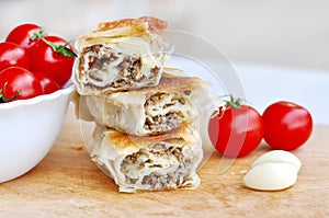 Delicious savory strudel stuffed with pork meat served on a wooden plate,with garlic and tomato cherry