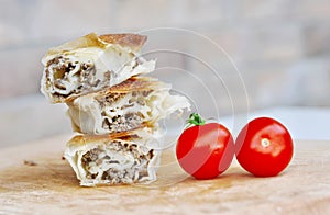 Delicious savory strudel stuffed with pork meat served on a wooden plate,with garlic and tomato cherry