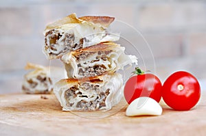 Delicious savory strudel stuffed with pork meat served on a wooden plate,with garlic and tomato cherry