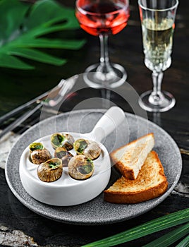 Delicious sea snails with herbs and bread on plate over marble background with drinks. Gourmet food. Escargot Snails, top view