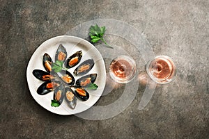 Delicious seafood mussels with spices, parsley and two glasses of pink sparkling wine in a row, dark rustic background. Top view,