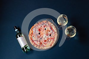 Delicious seafood pizza, bottle of white wine and glasses of white wine on dark background