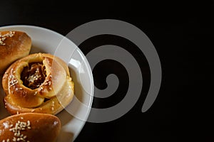 Delicious sesame buns or pies on white plate standing on black wooden table background