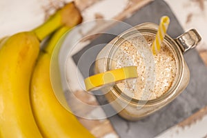 Delicious shake in cup with slices of fruit near bananas and cinnamon