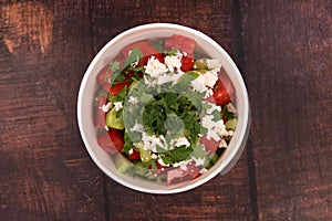 Delicious shopska salad with tomatoes cucumber, cheese and parsley in a bowl on a wooden table