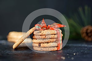 Delicious shortbread cookies with pieces of chocolate, with red ribbon, a sprig of spruce, Santa`s hat, a shortie on a dark photo