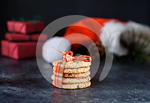 Delicious shortbread cookies with pieces of chocolate, with red ribbon, a sprig of spruce, Santa`s hat, a shortie on a dark photo