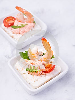 Delicious shrimp canapes with tomato and arugula on a light background. Festive appetizer with seafood.
