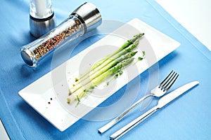 Delicious side dish for main courses - boiled asparagus with microgreen in a white plate on a blue tablecloth