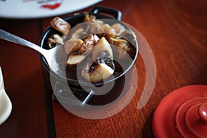 Delicious sliced mushroom cooked in a black pot, served hot with a spoon on a wooden table. Vegetarian plate side dishes in