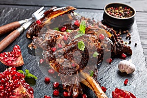 Delicious slow cooked leg of lamb with pomegranate seeds, mint leaves, spices and rosemary on a black slate plate on a wooden