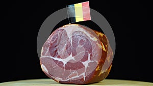 Delicious smoked tenderloin with small flag of Belgium, piece of meat rotating on balck background.