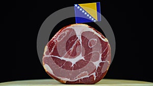 Delicious smoked tenderloin with small flag of Bosnia and Herzegovina, piece of meat rotating on balck background.