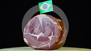 Delicious smoked tenderloin with small flag of Brazil, piece of meat rotating on balck background.