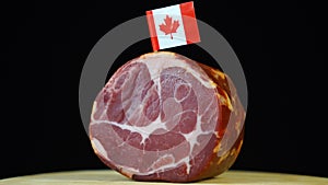 Delicious smoked tenderloin with small flag of Canada, piece of meat rotating on balck background.