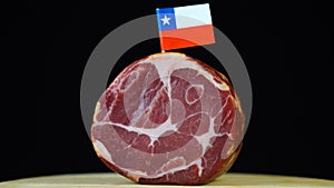 Delicious smoked tenderloin with small flag of Chile, piece of meat rotating on balck background.