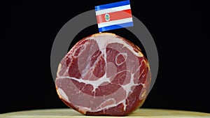 Delicious smoked tenderloin with small flag of Costa Rica, piece of meat rotating on balck background.