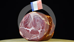 Delicious smoked tenderloin with small flag of France, piece of meat rotating on balck background.